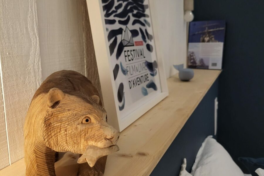 Ours en bois sculpté tenant un poisson dans sa gueule devant une affiche représentant une vague et un glacier