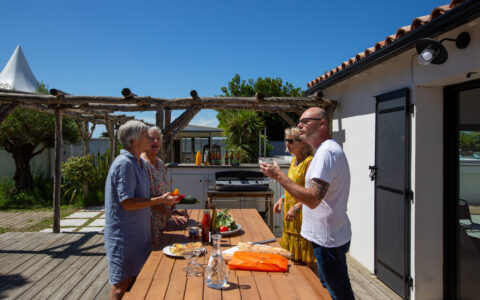 Quatre amis préparant un déjeuner à la plancha et profitant de la terrasse arrière ensoleillée